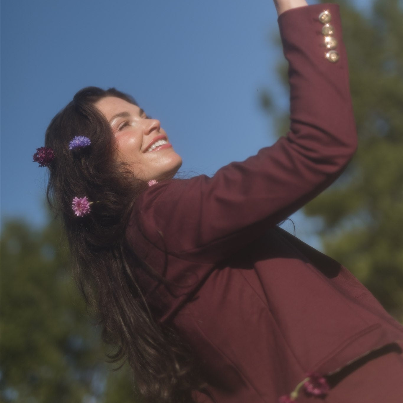 Woman in a burgundy coat reaching up towards the sky with a clear glass.