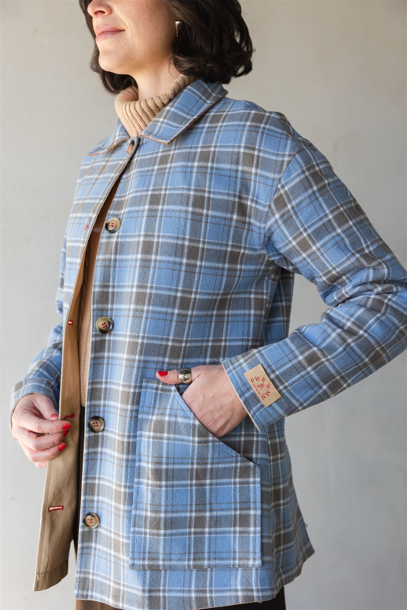 Person wearing a blue plaid barn coat with a beige interior and brown leather strap.