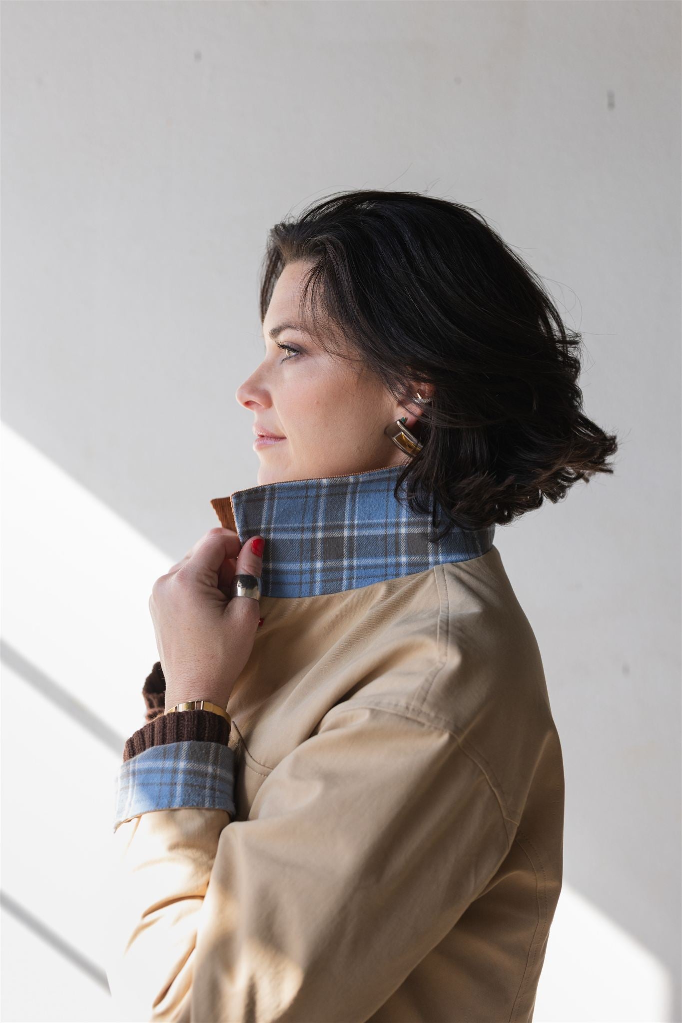 Woman wearing a beige barn coat with a plaid collar against a white wall power woman