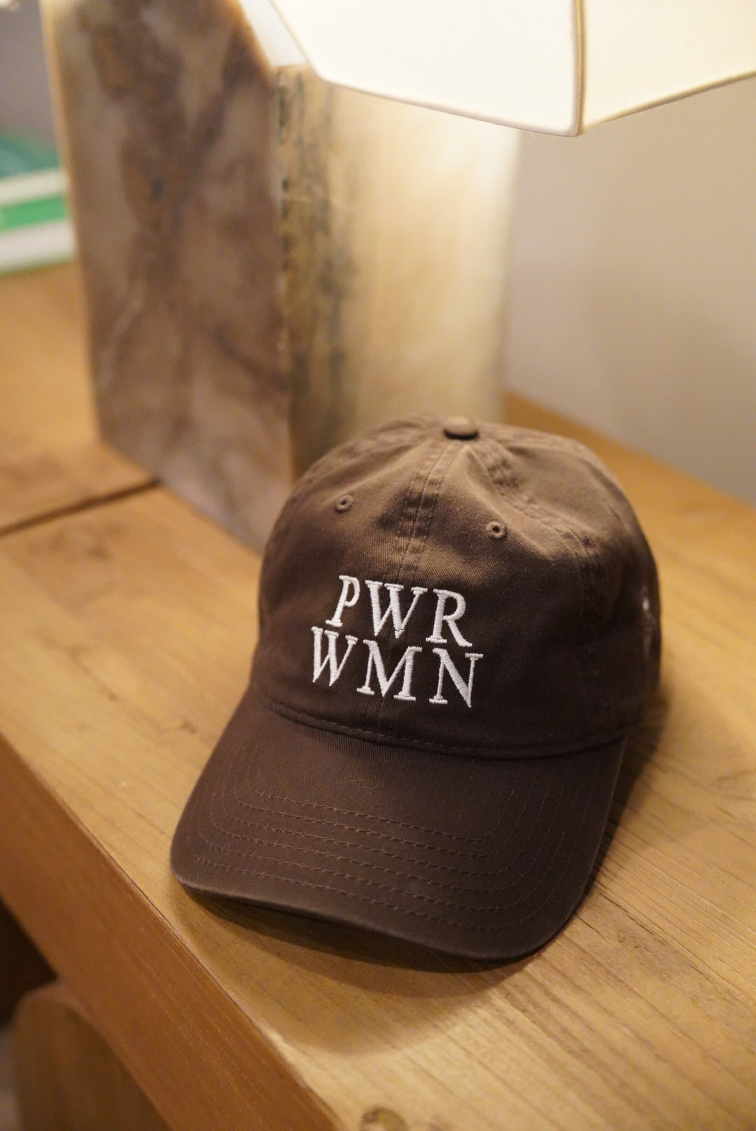 Brown cap with 'PWR WMN' text on a wooden surface
