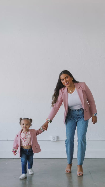 Mother and daughter walk hand in hand wearing matching custom pink blazers and jeans.